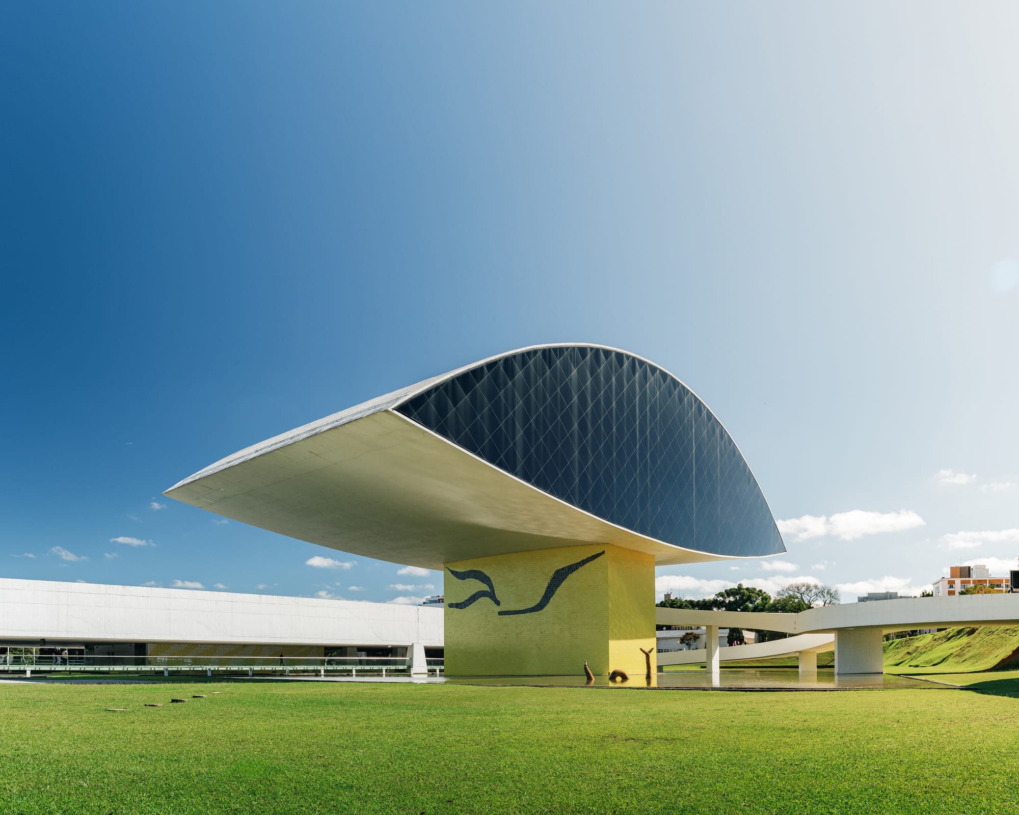 O olho do Museu Oscar Niemeyer sobre o gramado, contra céu limpo
