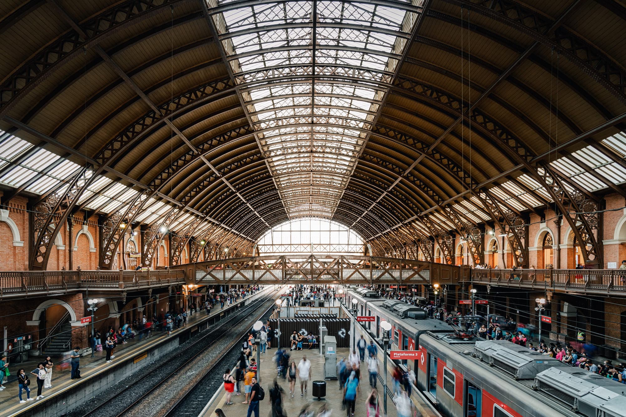 Interior de estação ferroviária com grande estrutura metálica em arco e plataformas ocupadas