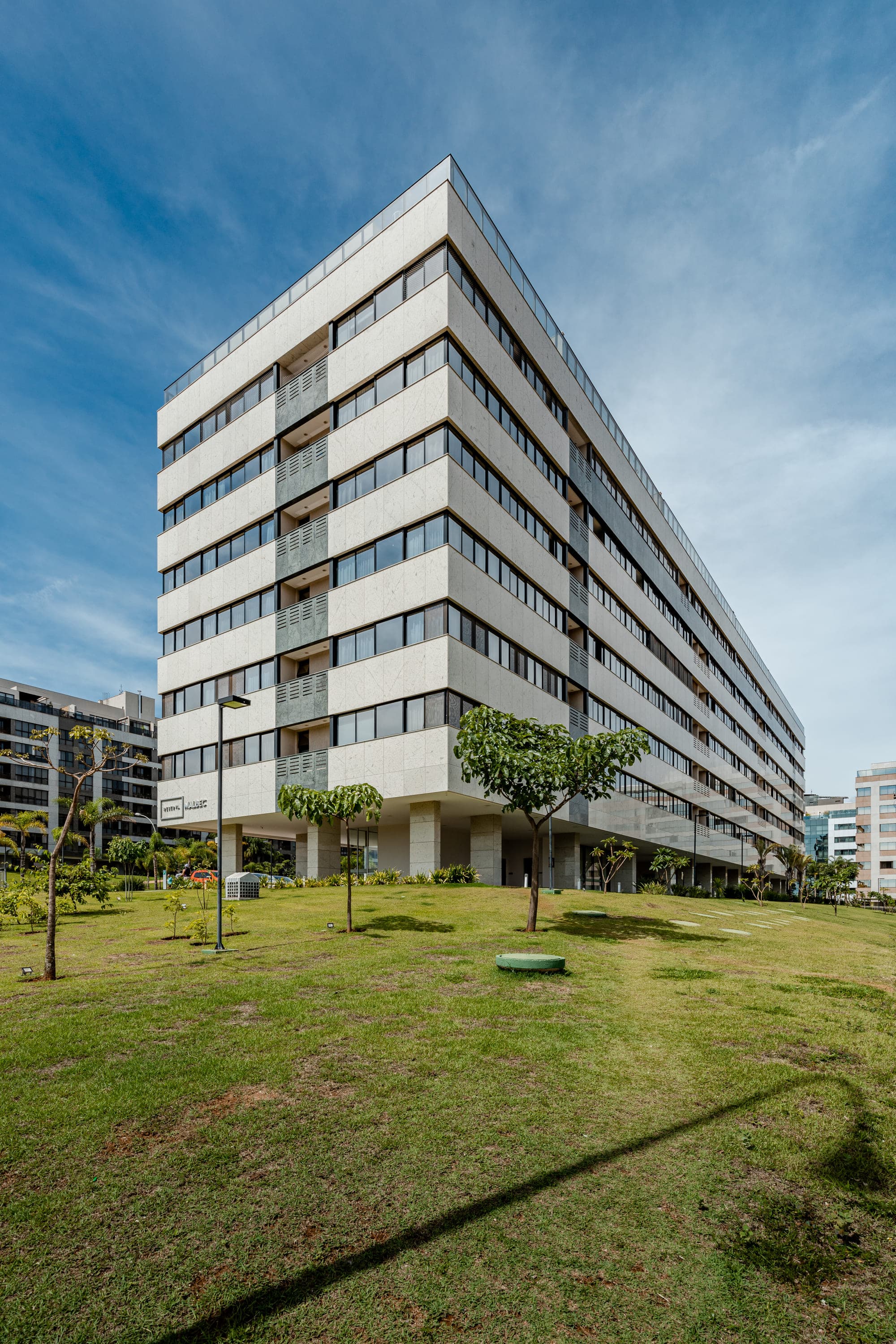 Edifício modernista de lâminas horizontais visto do gramado, com árvores em primeiro plano
