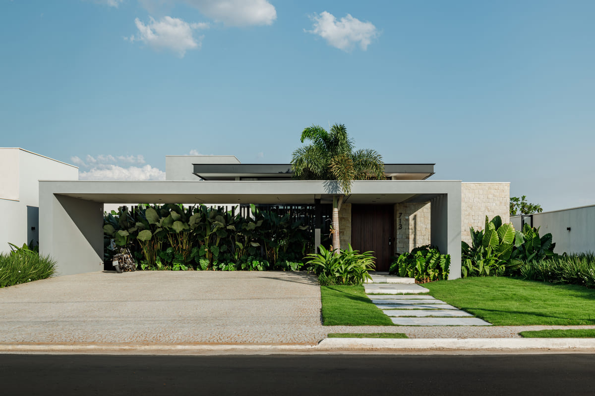 Fachada de casa com marquise em concreto, palmeira central e caminho de pedra no gramado
