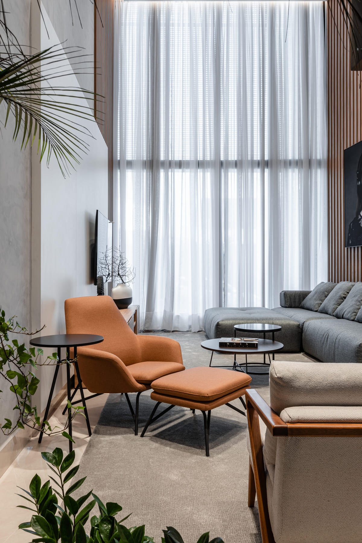 Sala de estar com cortina clara, poltrona de couro caramelo e sofá cinza