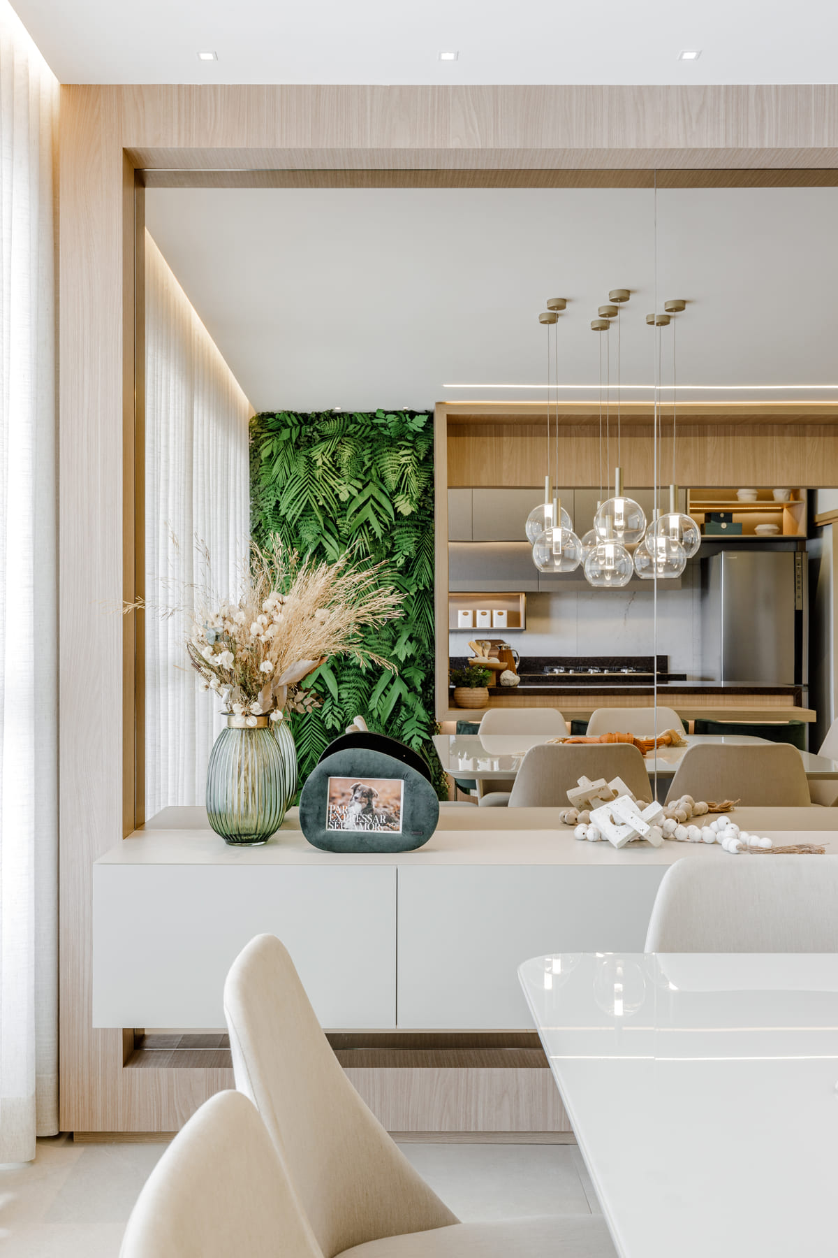Cozinha integrada com bancada branca, jardim vertical e pendentes de vidro